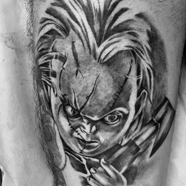 Black and grey Chucky tattoo with intense shading, featuring his stitched face, piercing stare, and a raised hammer for a menacing horror look.