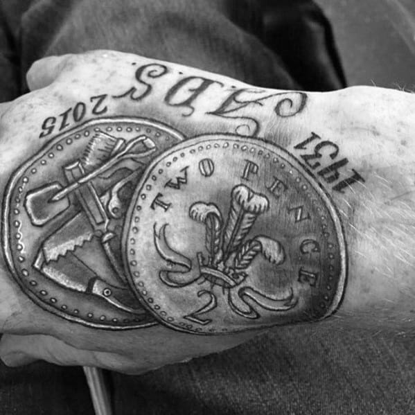 Realistic tattoo of overlapping coins, including a Two Pence piece, detailed with fine shading and lettering across the hand.