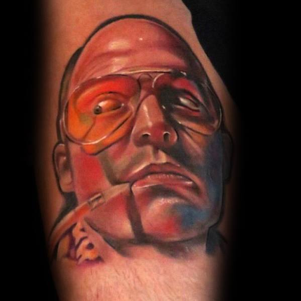 Hyper-realistic Hunter S. Thompson tattoo featuring his intense gaze, aviator glasses with an orange tint, and a cigarette, with bold shading.
