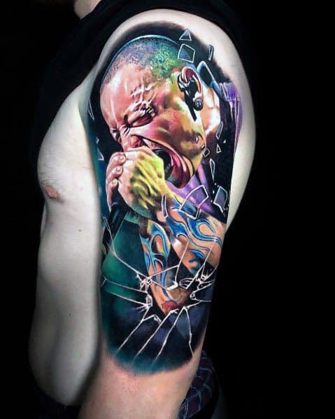 Hyper-realistic color tattoo of Chester Bennington screaming into a mic, featuring shattered glass effects and his iconic flame wrist tattoo.