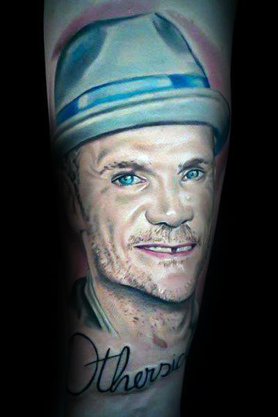 Realistic portrait tattoo featuring a smiling man wearing a fedora, with intricate shading and lifelike details, accented by script lettering below.