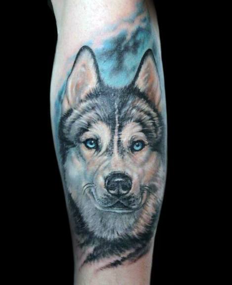 Realistic Siberian Husky tattoo on a man's leg, featuring lifelike fur details, piercing blue eyes, and a soft blue sky background for depth.