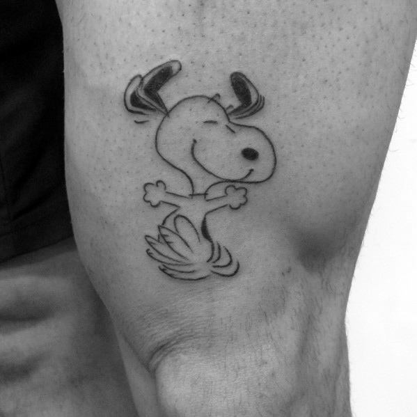 Black and white tattoo of Snoopy joyfully dancing with his ears up and arms out, placed on a person's leg.
