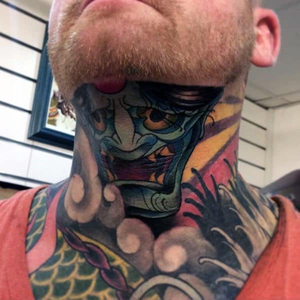 Throat tattoo featuring a fierce, colorful demon mask with intense shading, bold outlines, and dynamic background elements