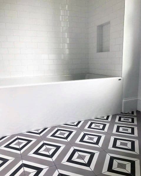Bathroom with white tub, grey subway tiles, and geometric patterned floor tiles