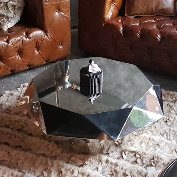 Geometric chrome coffee table in a living room with leather tufted sofas and fur rug.