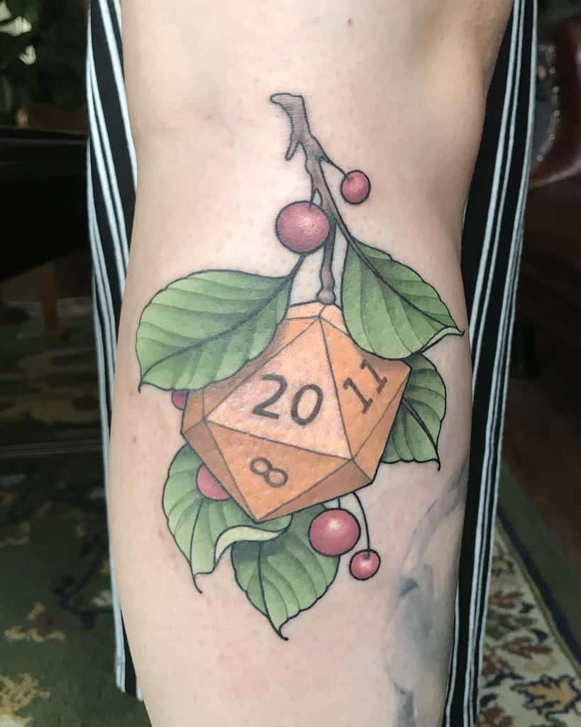 Delicate D20 dice tattoo nestled among vibrant green leaves and cherries, offering a whimsical and nature-inspired design