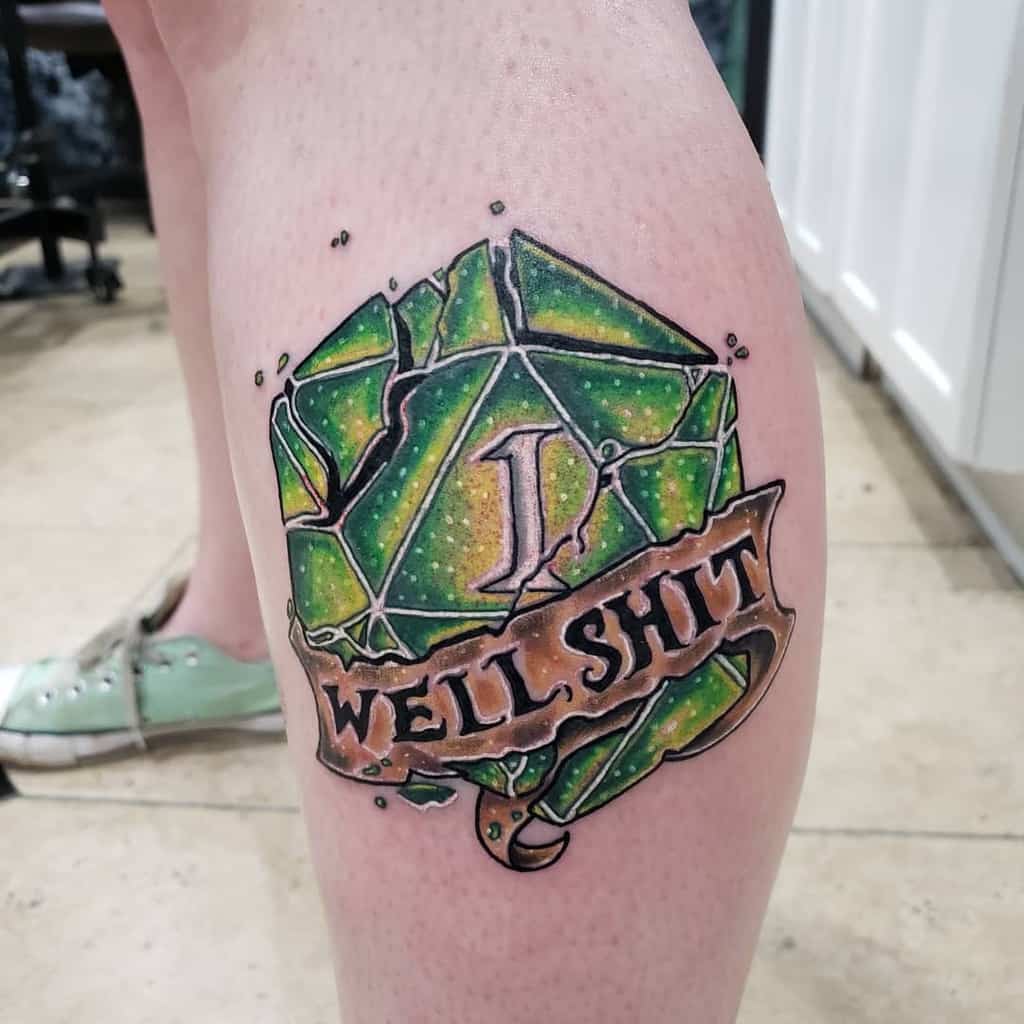 Humorous tattoo featuring a green shattered D20 dice with a natural 1, paired with a banner reading 'Well Shit' in bold lettering