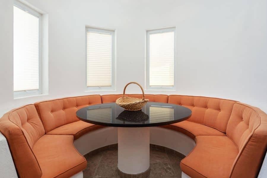 Round dining area with orange half-circle couch and black glass-top table.