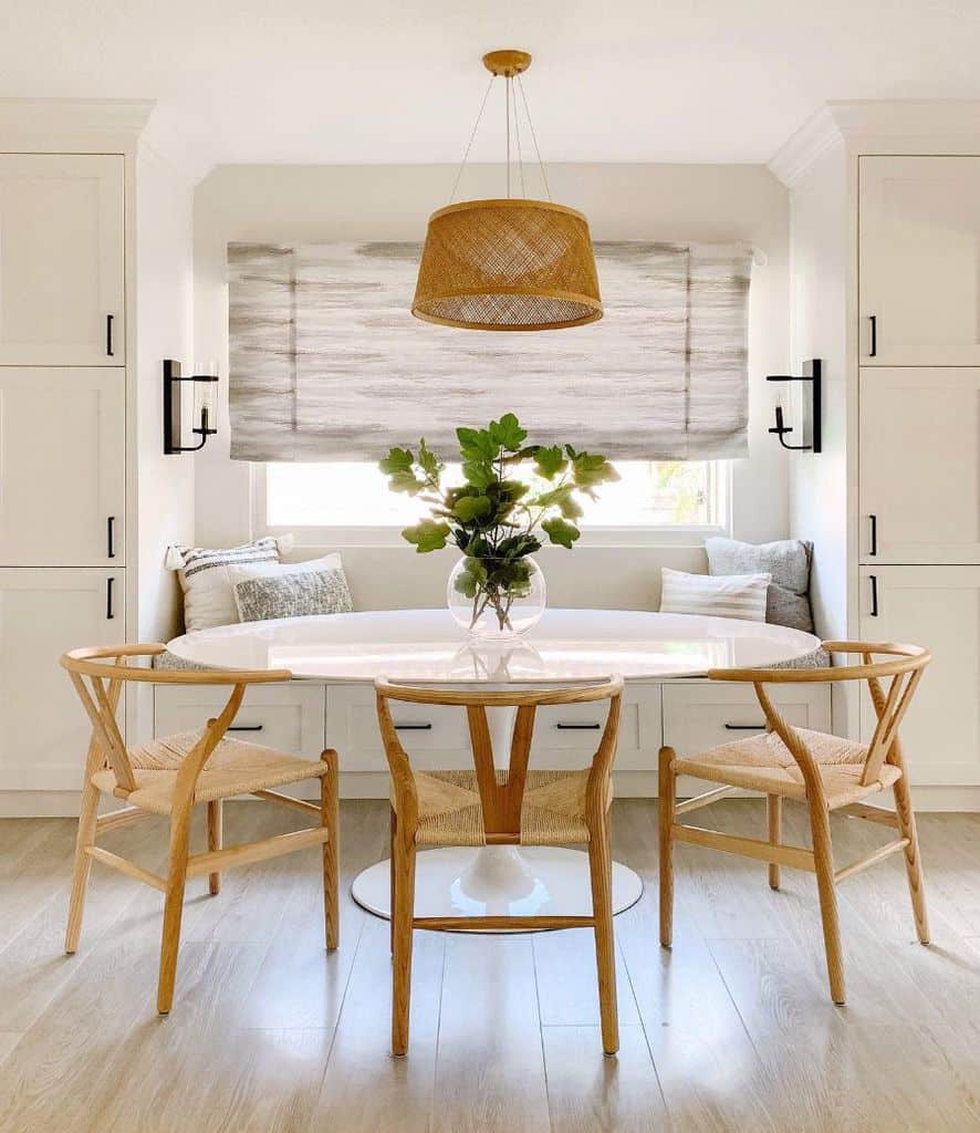 Modern dining area with white round table, wicker chairs, and built-in bench seating with cushions.