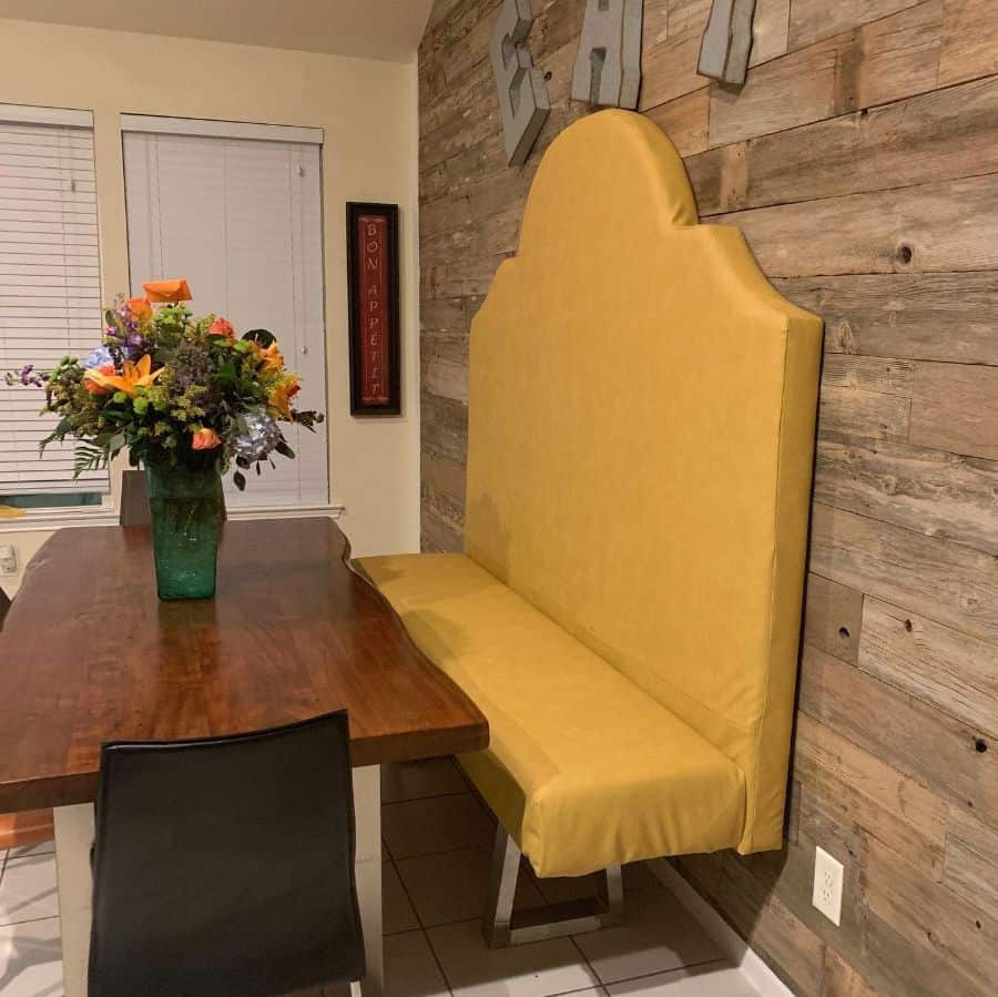 Dining area with tall yellow banquette seating, wooden table, and rustic wood wall decor.
