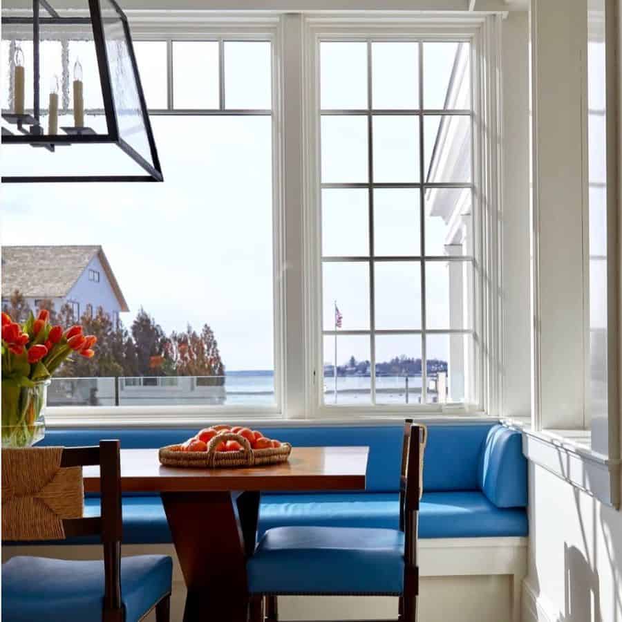Bright dining nook with blue banquette seating, wooden table, and large windows with ocean view.
