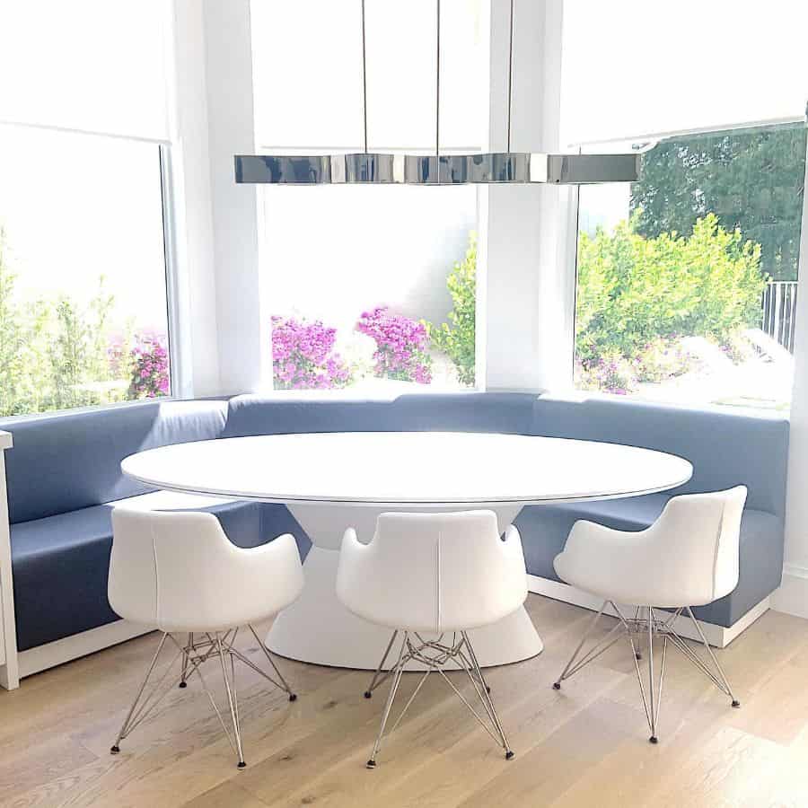 Modern dining area with round white table, blue banquette seating, and white chairs in a bright space.