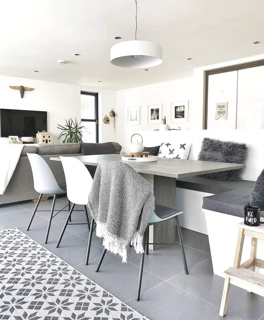 Modern white kitchen with grey tiled floor, cozy banquette seating, and sleek dining table.
