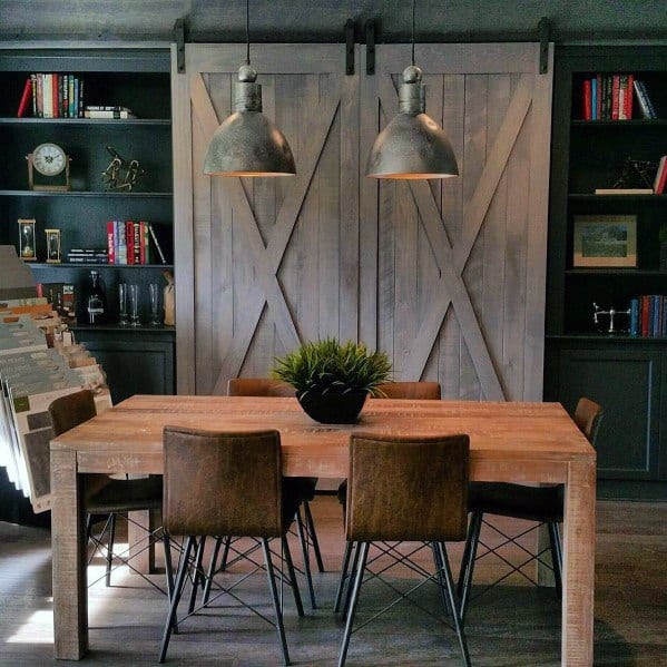 Rustic dining room with built-in bookcases, barn-style sliding doors, industrial pendant lights, and a wooden table