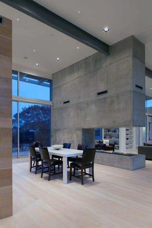 Modern dining room with a large concrete double-sided fireplace and minimalist decor.