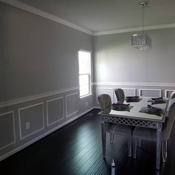 Modern dining room with gray walls, white chair rail molding, dark wood flooring, and a stylish crystal chandelier