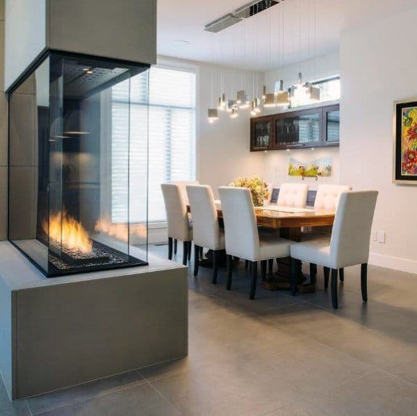 Modern dining area with glass-enclosed fireplace, wooden table, and elegant white chairs.