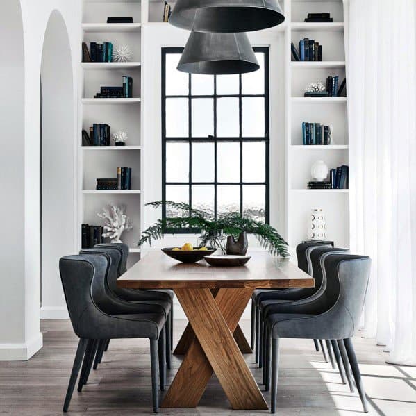 Modern dining room with wooden table, gray chairs, and a large window framed by bookshelves
