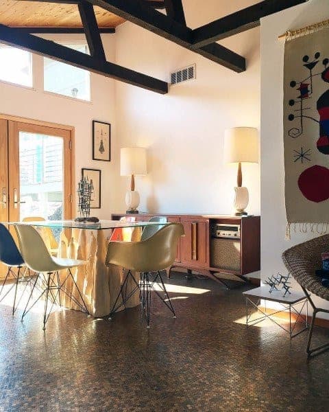 Mid-century modern dining room with penny tile floor, glass table, and colorful chairs.