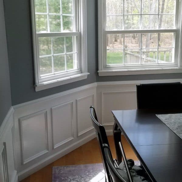 Bright dining area with white chair rail molding, gray walls, and large windows overlooking a serene outdoor view