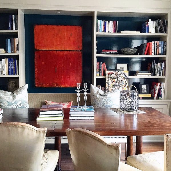 Elegant dining room with built-in bookcases, bold red artwork, wooden table, and plush upholstered chairs