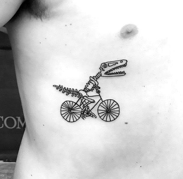 A minimalist black ink tattoo of a T-Rex skeleton riding a bicycle, blending humor with a creative and skeletal design on the ribcage.