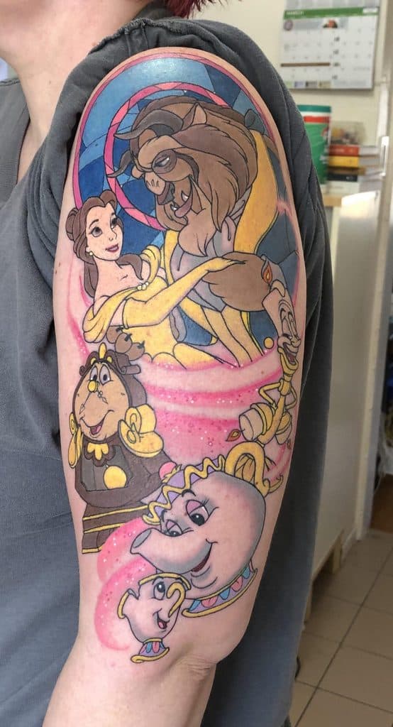 Colorful upper arm tattoo featuring Belle and the Beast dancing, with Cogsworth, Lumière, Mrs. Potts, and Chip surrounded by swirling pink magic.