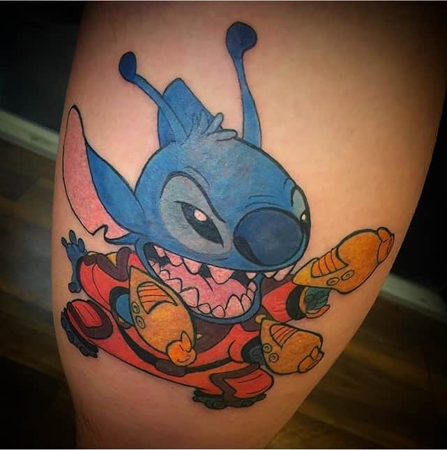 Colorful tattoo of Stitch from Lilo & Stitch in a red outfit, holding blasters, with an excited expression, on the thigh.