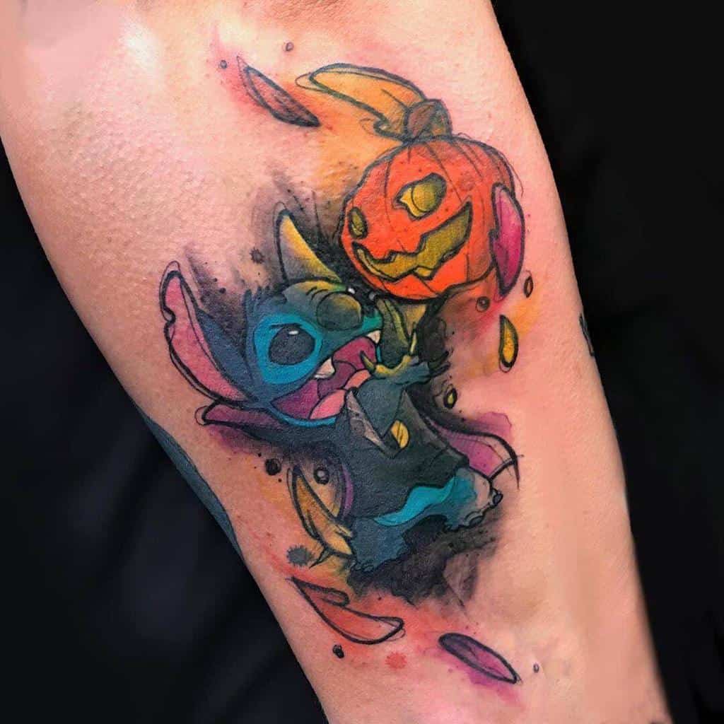 Colorful tattoo of Stitch from Lilo & Stitch in a costume, holding a jack-o'-lantern, with vibrant watercolor splashes, on the forearm.