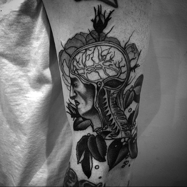 Black and grey tattoo of a human head cross-section with brain and spine exposed, surrounded by botanical and insect elements.