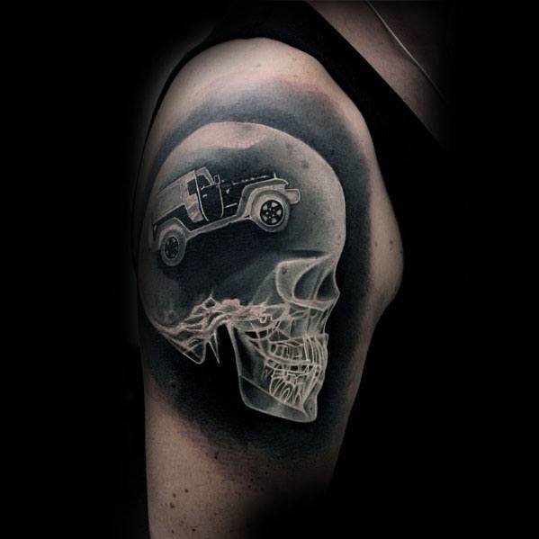 Black and grey Jeep tattoo on the upper arm, featuring a surreal design of a Jeep inside a translucent skull, blending realism with creative shading.