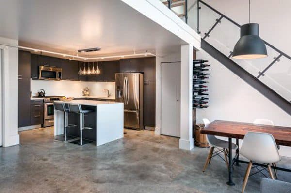 Minimalist loft kitchen with modern appliances, concrete floor, and dining area under staircase.