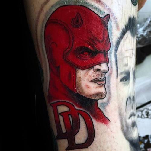 Bold Daredevil profile tattoo in classic red with the DD logo below, featuring sharp outlines and intense expression.