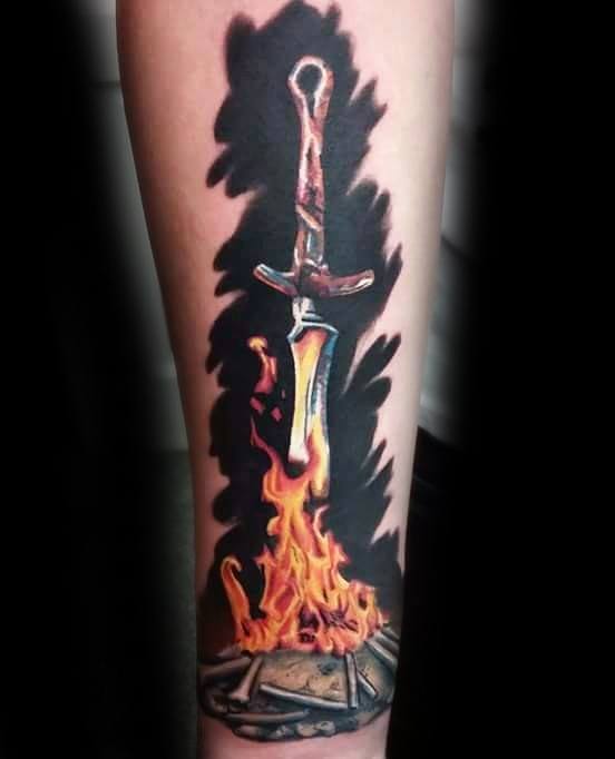 Dark Souls bonfire tattoo with a sword engulfed in vivid flames, set against a dark smoky background on the forearm.