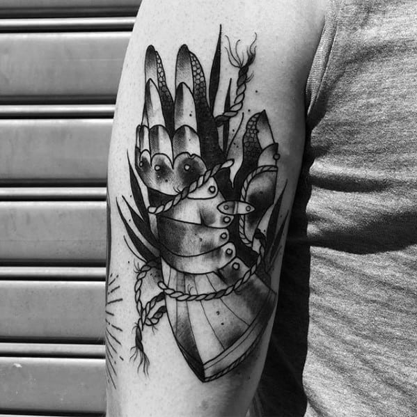 Black and grey tattoo of an armored hand with fingers extended, surrounded by leaves and rope details, inked on the upper arm.