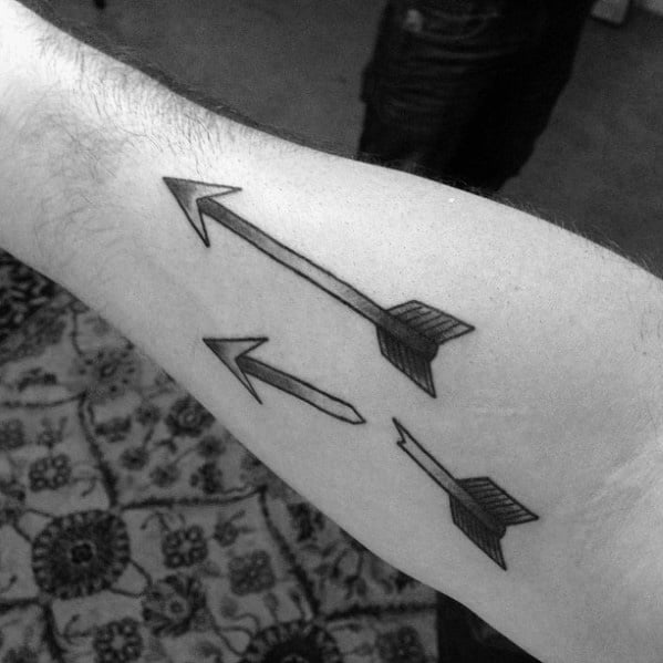 Minimalist blackwork tattoo of a broken arrow in three segments, each piece aligned diagonally along the inner forearm.