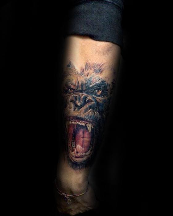 Vibrant color tattoo of King Kong roaring fiercely, inked on the forearm with detailed red mouth and intense glowing eyes.