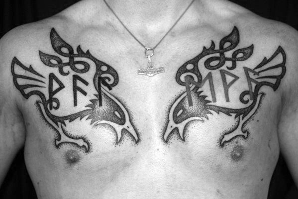 Bold Nordic-style chest tattoo of Huginn and Muninn with runes, mirrored across both pectorals in tribal raven designs.