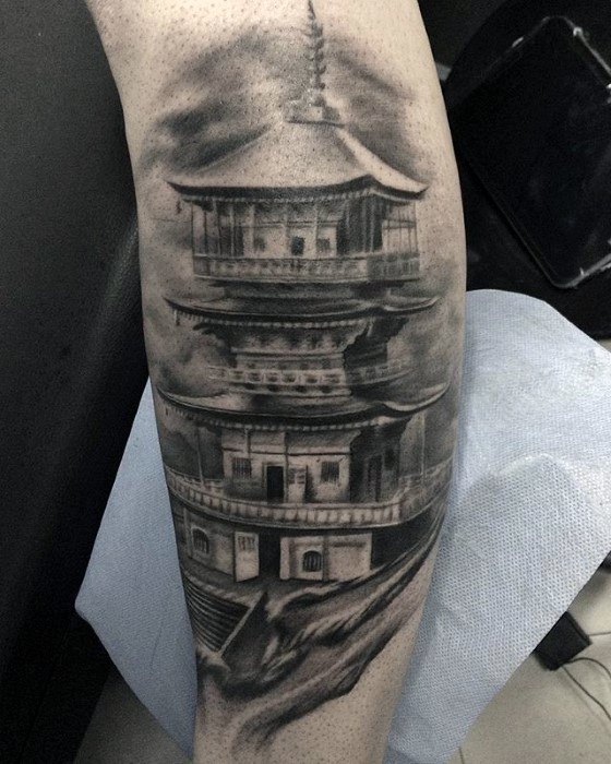 Black and grey tattoo of a multi-tiered Japanese pagoda on a rocky cliff with misty clouds for a mysterious, dramatic effect.