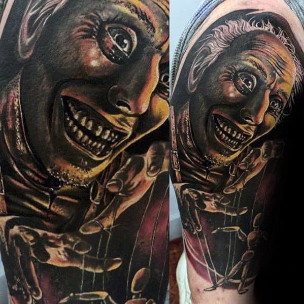Creepy puppet master tattoo featuring a grinning, wide-eyed face controlling strings, with dark tones and intense expression.