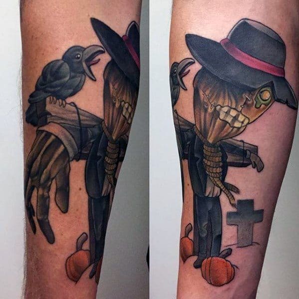 Stylish scarecrow tattoo with stitched smile, black hat, red band, glowing eye, crow, pumpkins, and a grave cross in the background.