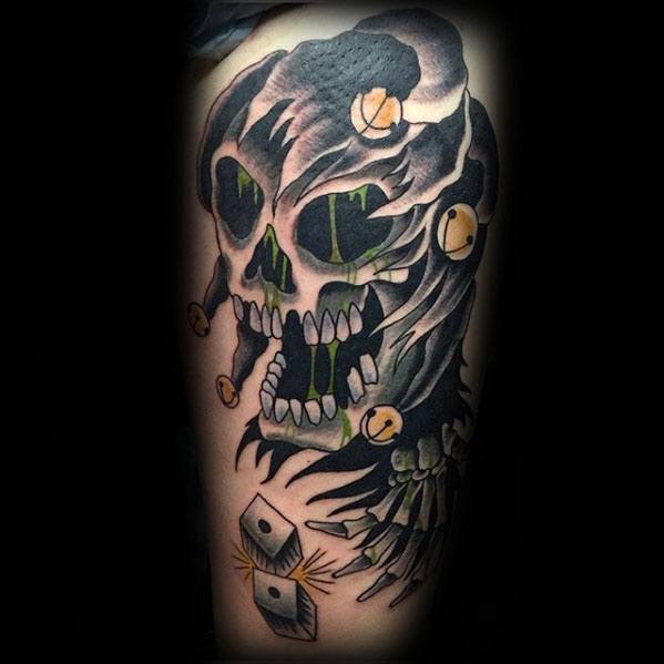 A bold black and green tattoo of a skull wearing a jester hat, with dice below and flowing details that create a dynamic, eerie effect.