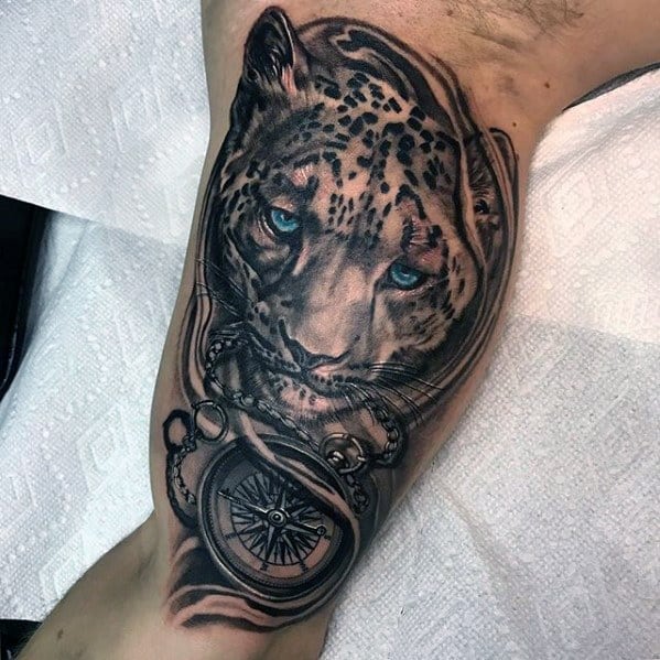 Snow leopard tattoo with piercing blue eyes, paired with a detailed compass on the bicep, symbolizing direction and inner strength.