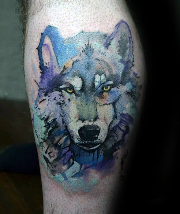 Realistic wolf tattoo with piercing yellow eyes and soft watercolor shades of blue, purple, and gray for a fierce, dreamy effect.