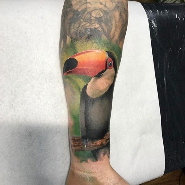 Realistic toucan tattoo with vibrant orange beak and lush green background, perched on a branch on the calf.