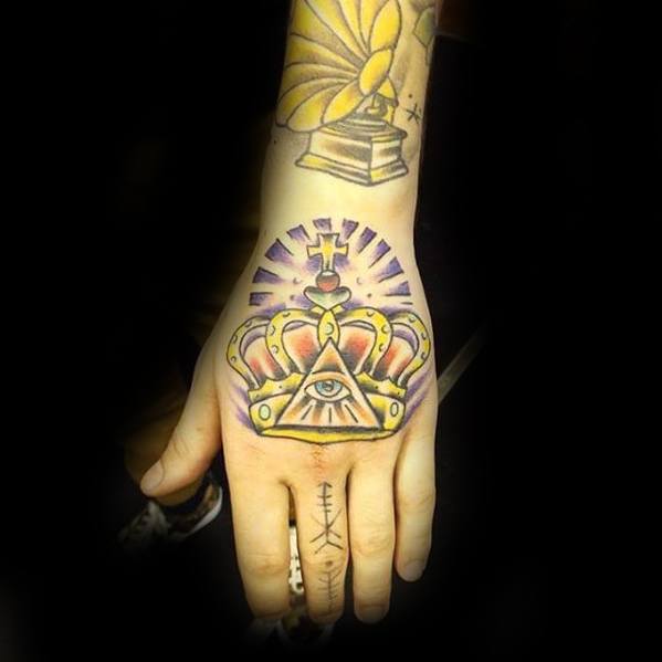 Vibrant hand tattoo of a crowned all-seeing eye inside a triangle with purple rays and golden accents in a bold traditional style.
