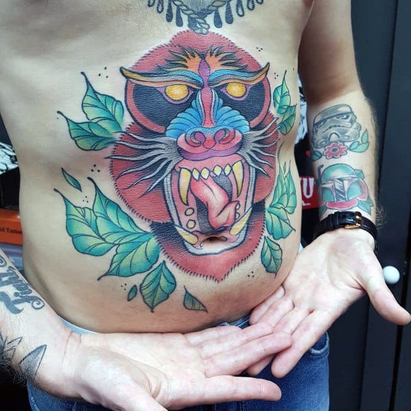 Neo-traditional baboon stomach tattoo with bold colors, fierce expression, glowing eyes, and jungle leaves for a striking and dynamic design.
