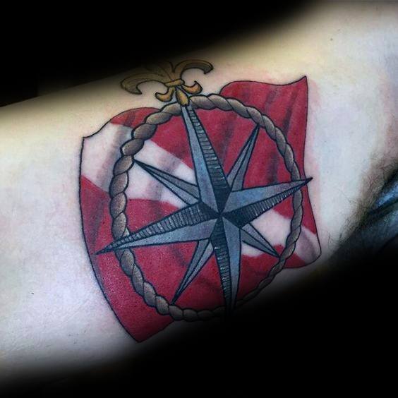 Tattoo of a nautical compass over a red and white dive flag, framed by a rope border, symbolizing guidance, adventure, and love for the ocean.