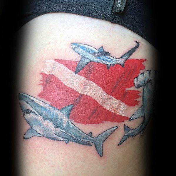 Tattoo of three sharks, including a hammerhead, swimming around a red and white dive flag, representing a passion for scuba diving and marine life.